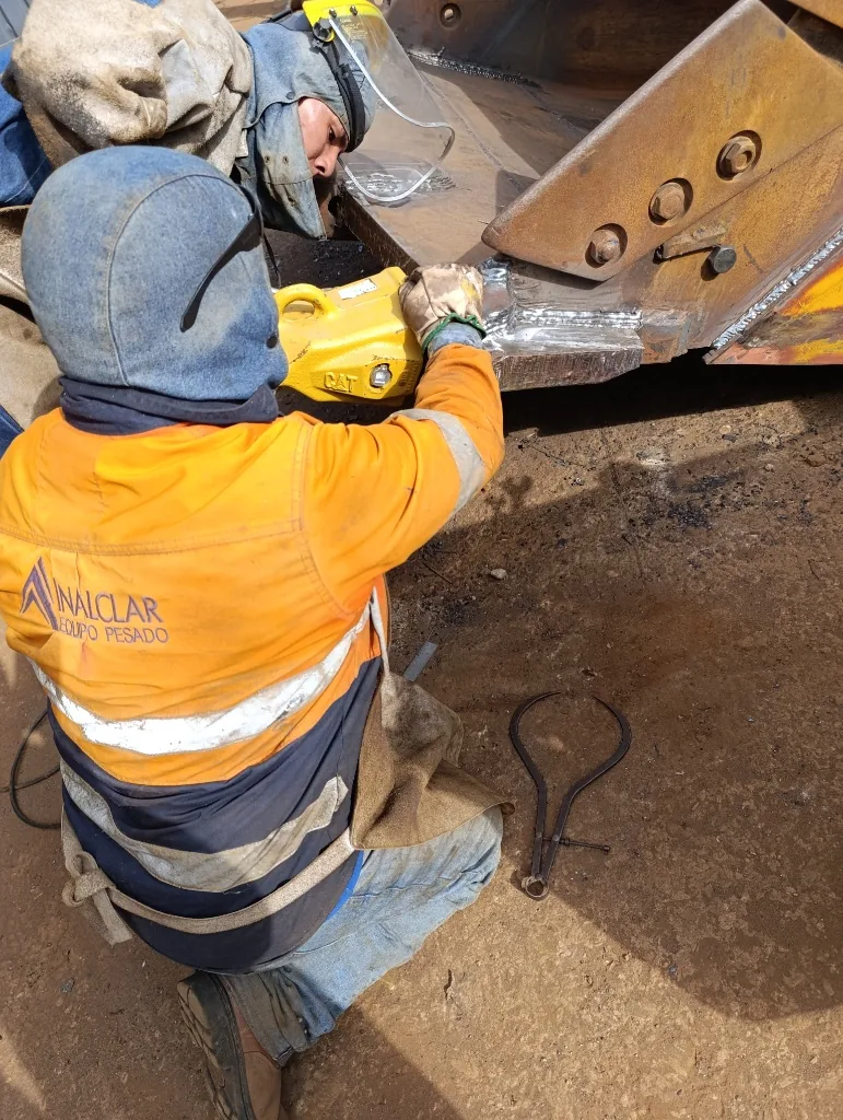 Técnico con equipo de protección aplicando soldadura en cantonera de balde de excavación